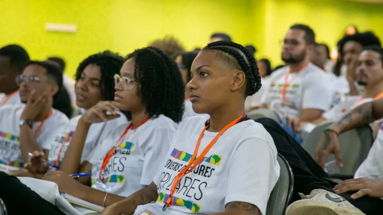 Jovens negras, vestindo a camiseta de Jovens Defensores Populares, sentadas como se ouvissem uma palestra.