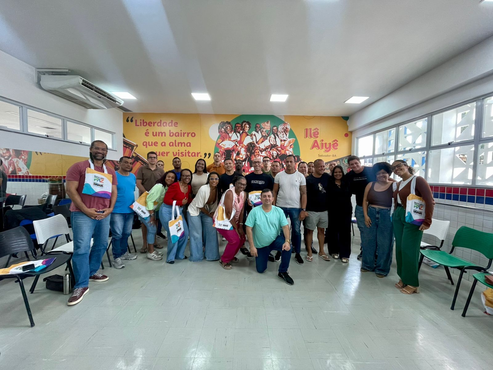 Turma posando para foto, em frente a um banner do Ile Aiyê