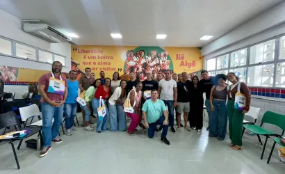 Turma posando para foto, em frente a um banner do Ile Aiyê