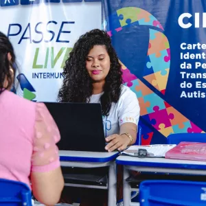 Mulher parda, de cabelos compridos, realizando atendimento.