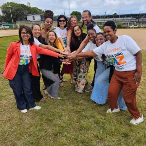 Grupo de pessoas em um terreno, ao ar livre, juntando as mãos em símbolo de parceria.