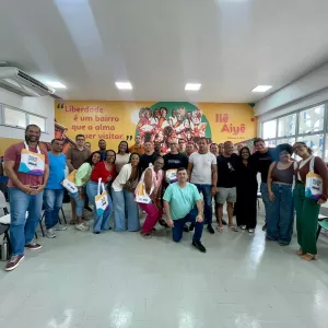 Turma posando para foto, em frente a um banner do Ile Aiyê