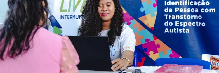 Mulher parda, de cabelos compridos, realizando atendimento.