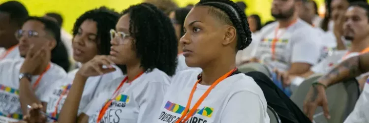Jovens negras, vestindo a camiseta de Jovens Defensores Populares, sentadas como se ouvissem uma palestra.