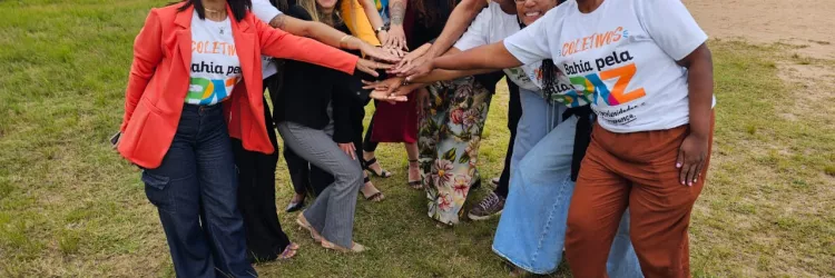 Grupo de pessoas em um terreno, ao ar livre, juntando as mãos em símbolo de parceria.