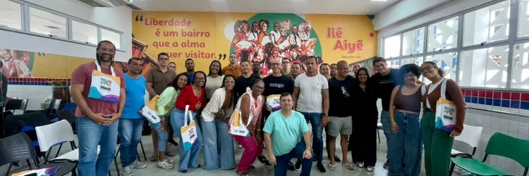 Turma posando para foto, em frente a um banner do Ile Aiyê