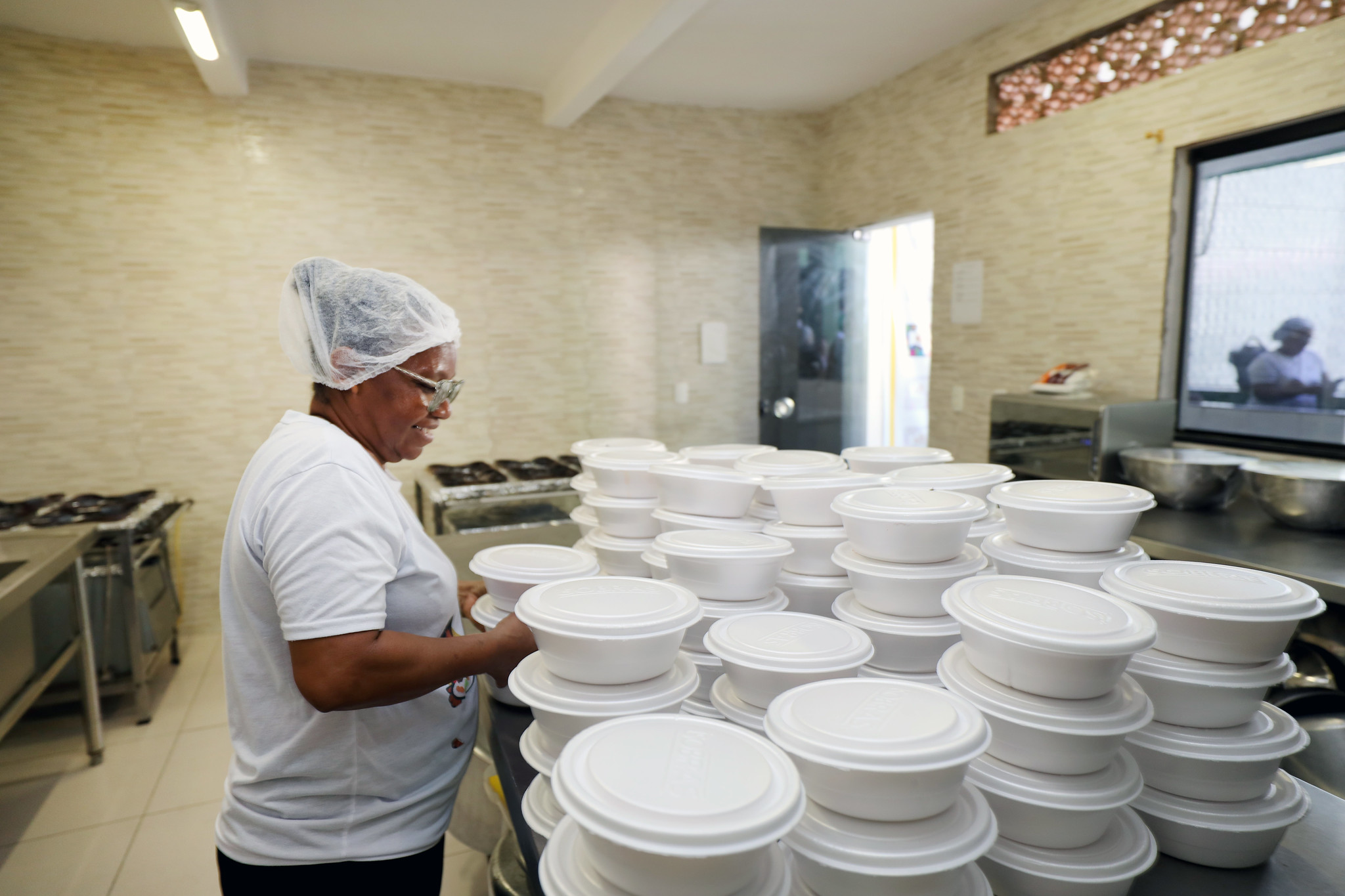 imagem de cozinheira organizando várias marmitas na cozinha comunitária 