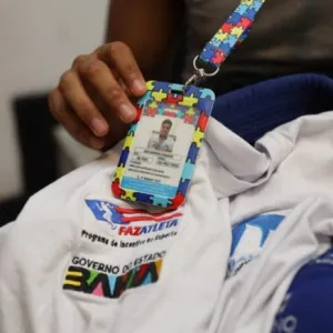 Foto de camisa do programa e mão de atleta segurando o crachá 