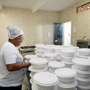 imagem de cozinheira organizando várias marmitas na cozinha comunitária 