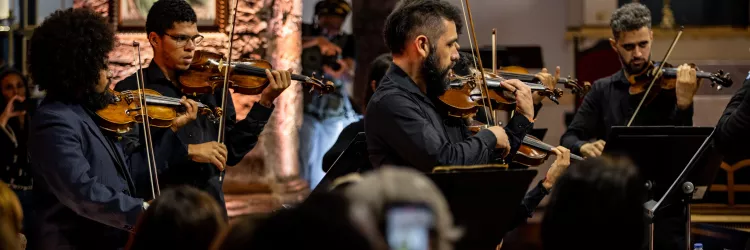 OSBA leva música clássica e poesia à Feira Literária de Mucugê em concerto gratuito neste sábado (16)     Apresentação integra a programação da Fligê 2025 e acontecerá na Igreja Matriz, às 19h; programa terá obras de Bach e Mozart, além de poemas de Gregório de Matos    Site---Osba-na-Estrada---FLIGÊ---VOZES-DO-SAGRADO.png   A Orquestra Sinfônica da Bahia (OSBA) vai até a região da Chapada Diamantina neste sábado, 16 de agosto, para uma apresentação especial que mescla música clássica e poesia dentro da pro