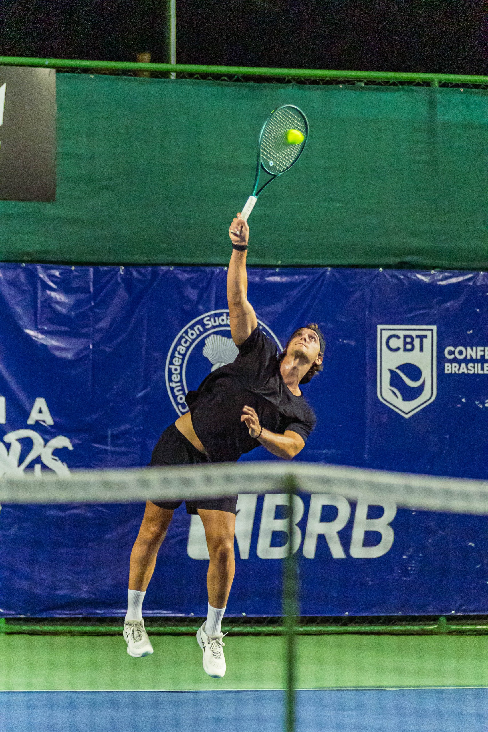 rapaz com a raquete de tênis dando um salto em direção para bater na bola 