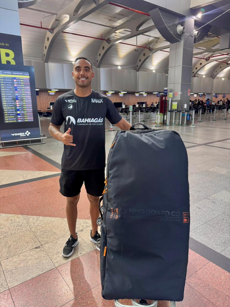 rapaz em pé no aeroporto, ao lado da sua mala 