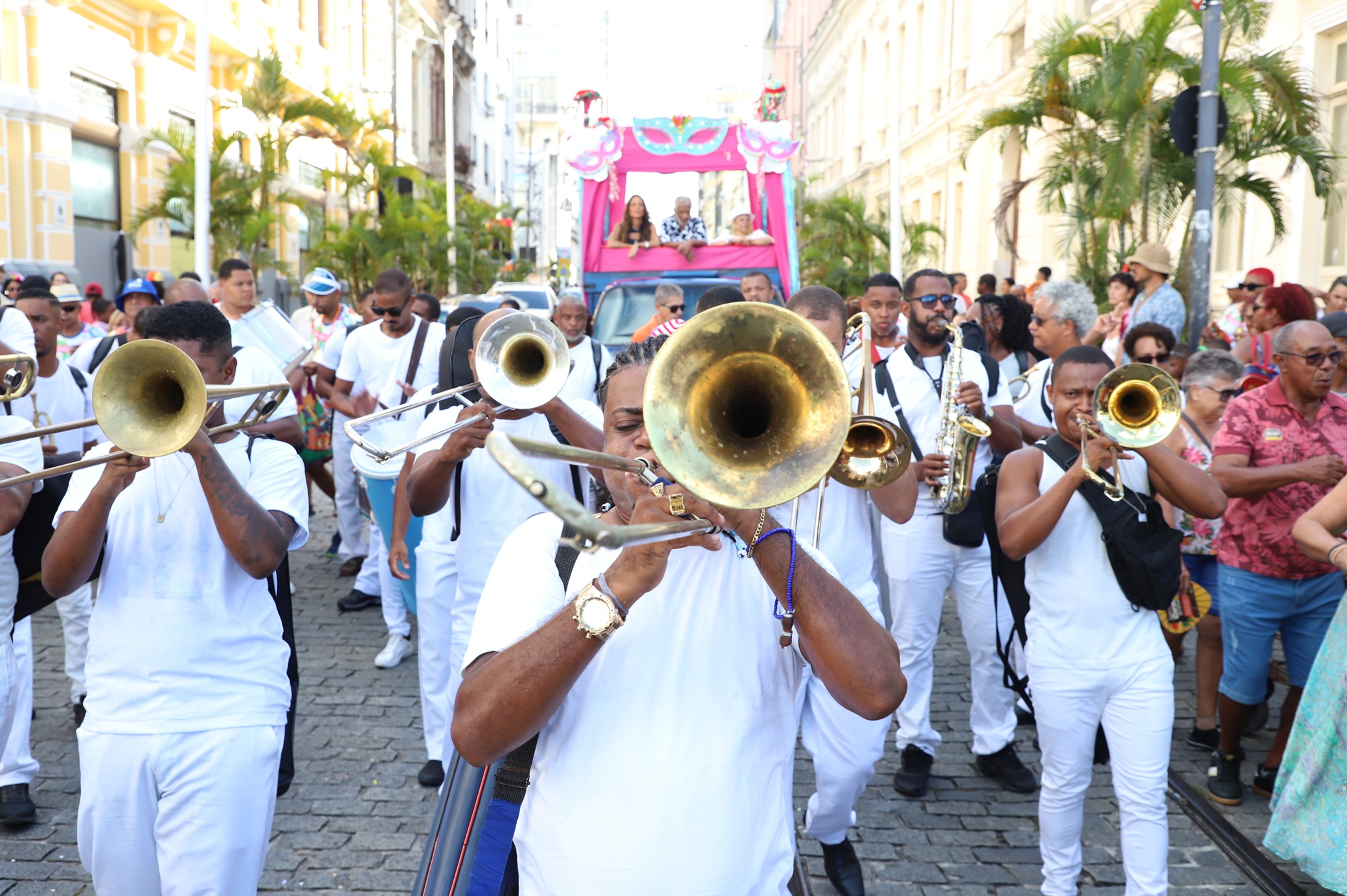 Vestidos de branco, os músicos da fanfarra Bandão Aurora puxam cortejo à frente do carro aberto
