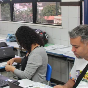 Emissão de CIPTEA na Caravana. Servidores da Sudef atendem a duas mulheres, ao fundo o cartaz com a logo da CIPTEA.