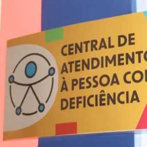Placa colorida da Central de Atendimento à Pessoa com Deficiência em ambiente iluminado.