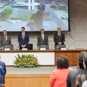 Posse PGU / SGCS / AGU -são duas imagens coladas, uma com a mesa, com pessoas vestidas de social e uma do secretário com a nova procuradora, ele veste terno azul e ela veste cinza. Eles sorriem. 
