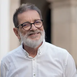 Paulo Miguez, homem branco, de barba branca, camisa branca e usando óculos