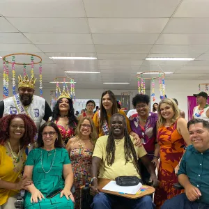 Pessoas reunidas, de roupas coloridas, num cenário carnavalesco. 