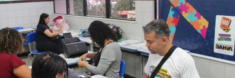 Emissão de CIPTEA na Caravana. Servidores da Sudef atendem a duas mulheres, ao fundo o cartaz com a logo da CIPTEA.