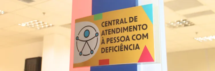 Placa colorida da Central de Atendimento à Pessoa com Deficiência em ambiente iluminado.