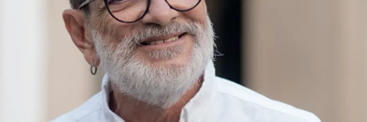 Paulo Miguez, homem branco, de barba branca, camisa branca e usando óculos