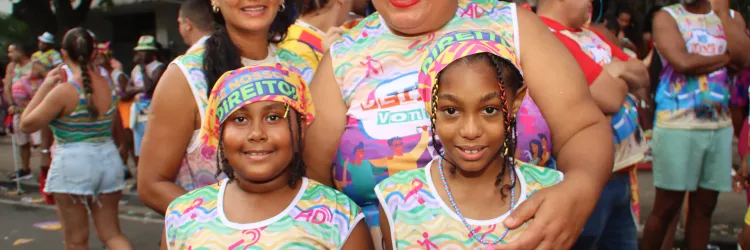 quatro epssoas na foto usando a camisa do bloco me deixe a vontade, nas cores azul, verde e laranja. uma dela usa uma bandana da campanha respeito é nosso direito. 