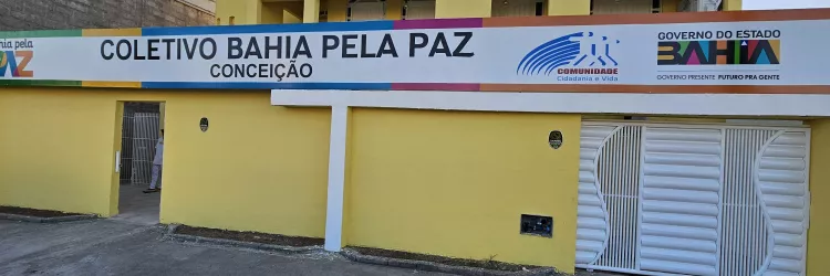 Faixada da unidade do Bahia Pela Paz de Feira. Muro na cor amarelo, com  portão branco. Acima do muro, uma placa grande escrito "coletivo bahia pela paz conceição", e ao lado, a logomarca do governo da bahia.