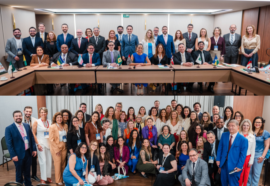 A imagem está dividida em duas partes. Na parte superior, um grupo de cerca de 25 pessoas, homens e mulheres, posa atrás de uma mesa em formato de “U”, decorada com pequenas bandeiras de estados brasileiros. Estão em trajes sociais, alguns sentados e outros em pé, olhando para a câmera. Na parte inferior, outro grupo maior, com mais de 40 pessoas, também em roupas sociais, reúne-se para foto em pé e agachados à frente. Todos sorriem em um ambiente de reunião formal com clima de confraternização.