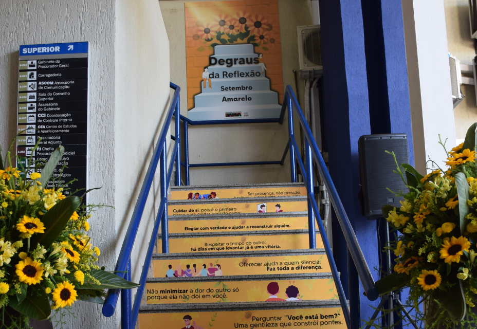 Escada decorada com frases de incentivo à empatia, escuta e cuidado emocional, como parte da campanha “Degraus da Reflexão – Setembro Amarelo”. Cada degrau traz uma mensagem positiva, estimulando atitudes simples que fazem a diferença no dia a dia. Ao fundo, há um painel com o nome da campanha.