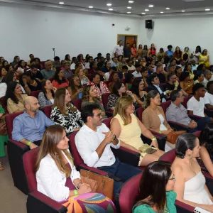 Auditório cheio, com muitas pessoas sentadas em poltronas vermelhas, assistindo ao evento