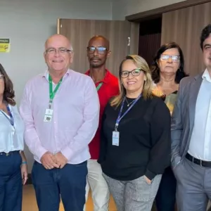 Um grupo de pessoas está reunido em um ambiente interno, posando para uma foto. Todas usam crachá e roupas formais ou de trabalho, indicando um contexto profissional ou institucional.