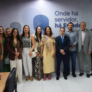 Grupo de pessoas posa para foto em frente a uma parede com a frase “Onde há servidor, há Estado”. Todos estão alinhados, sorrindo, em um registro formal de equipe ou evento institucional.