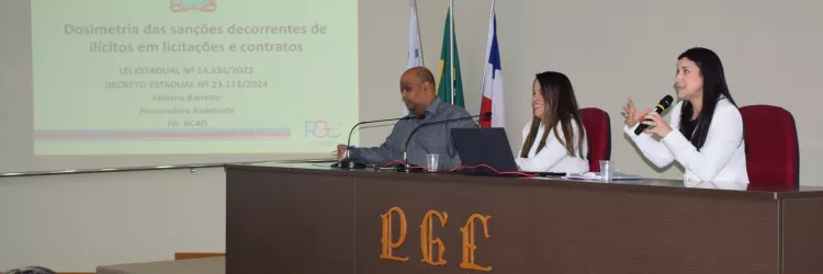 Na imagem, três pessoas estão sentadas atrás de uma mesa de auditório da PGE. À esquerda, um homem de camisa cinza olha para a frente. No centro, uma mulher de blazer branco sorri. À direita, outra mulher de blazer branco fala ao microfone com gestos expressivos. Atrás deles há quatro bandeiras. Na parede, um telão projeta o título da apresentação: “Dosimetria das sanções decorrentes de ilícitos em licitações e contratos”, com referência à lei estadual nº 14.634/2023 e ao decreto nº 23.113/2024.