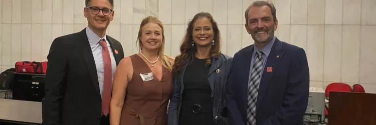 Quatro pessoas posam sorridentes em frente à parede com a inscrição “Senado Federal”. Estão bem-vestidas, demonstrando participação em um evento formal ou institucional. A imagem transmite profissionalismo, união e engajamento em atividades no ambiente legislativo.