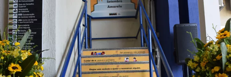 Escada decorada com frases de incentivo à empatia, escuta e cuidado emocional, como parte da campanha “Degraus da Reflexão – Setembro Amarelo”. Cada degrau traz uma mensagem positiva, estimulando atitudes simples que fazem a diferença no dia a dia. Ao fundo, há um painel com o nome da campanha.