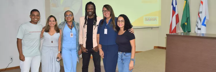 Foto em grupo com o palestrante e participantes ao final do workshop. Todos posam sorrindo em frente à tela de projeção que identifica o evento. A imagem registra o encerramento da atividade e o clima de integração entre os envolvidos.