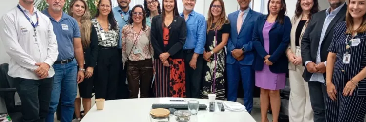 Foto posada do grupo após a reunião. Cerca de quinze pessoas ficam lado a lado sorrindo para a câmera. A mesa à frente tem copos e garrafas. Todos vestem roupas formais ou sociais em uma sala bem iluminada.