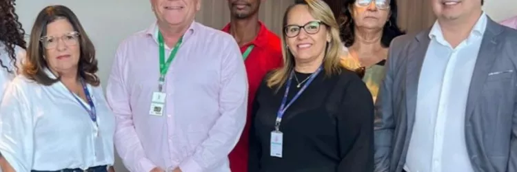 Um grupo de pessoas está reunido em um ambiente interno, posando para uma foto. Todas usam crachá e roupas formais ou de trabalho, indicando um contexto profissional ou institucional.