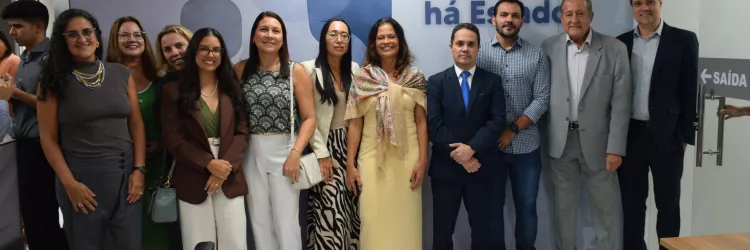 Grupo de pessoas posa para foto em frente a uma parede com a frase “Onde há servidor, há Estado”. Todos estão alinhados, sorrindo, em um registro formal de equipe ou evento institucional.
