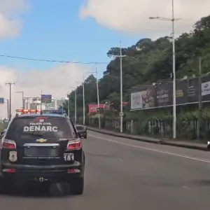 Viatura da Polícia Civil da Bahia, com identificação do DENARC, circula com sirenes ligadas por avenida de Salvador durante operação policial.