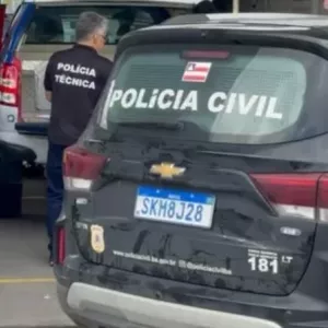 Viatura da Polícia Civil da Bahia estacionada em um posto, com agentes da Polícia Técnica ao fundo próximos a outra viatura, durante uma operação.