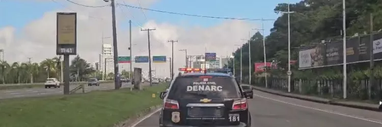 Viatura da Polícia Civil da Bahia, com identificação do DENARC, circula com sirenes ligadas por avenida de Salvador durante operação policial.
