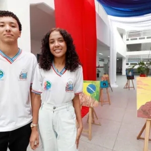 Dois jovens estudantes em frente a quadros em um colégio.