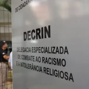 A imagem amostra uma placa escrito "Decrin, delegacia especializada de combate ao racismo e à intolerância religiosa"