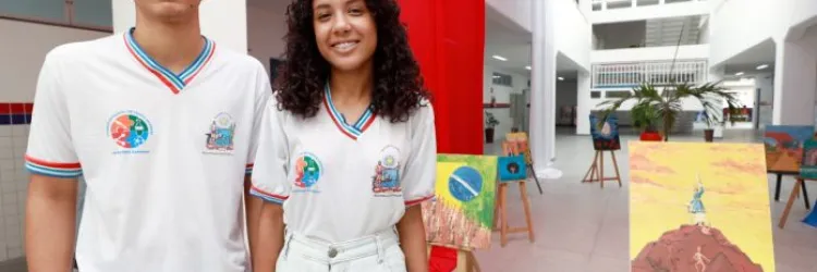 Dois jovens estudantes em frente a quadros em um colégio.